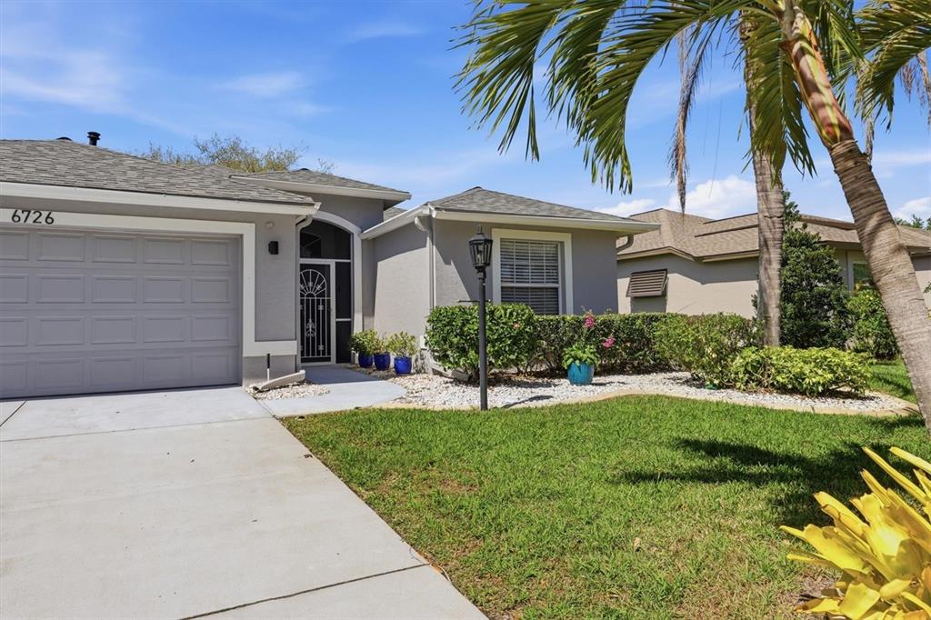 A gray single-story house features a two-car garage, a front entryway, and a palm tree — 6726 W COUNTRY CLUB LANE, SARASOTA, FL