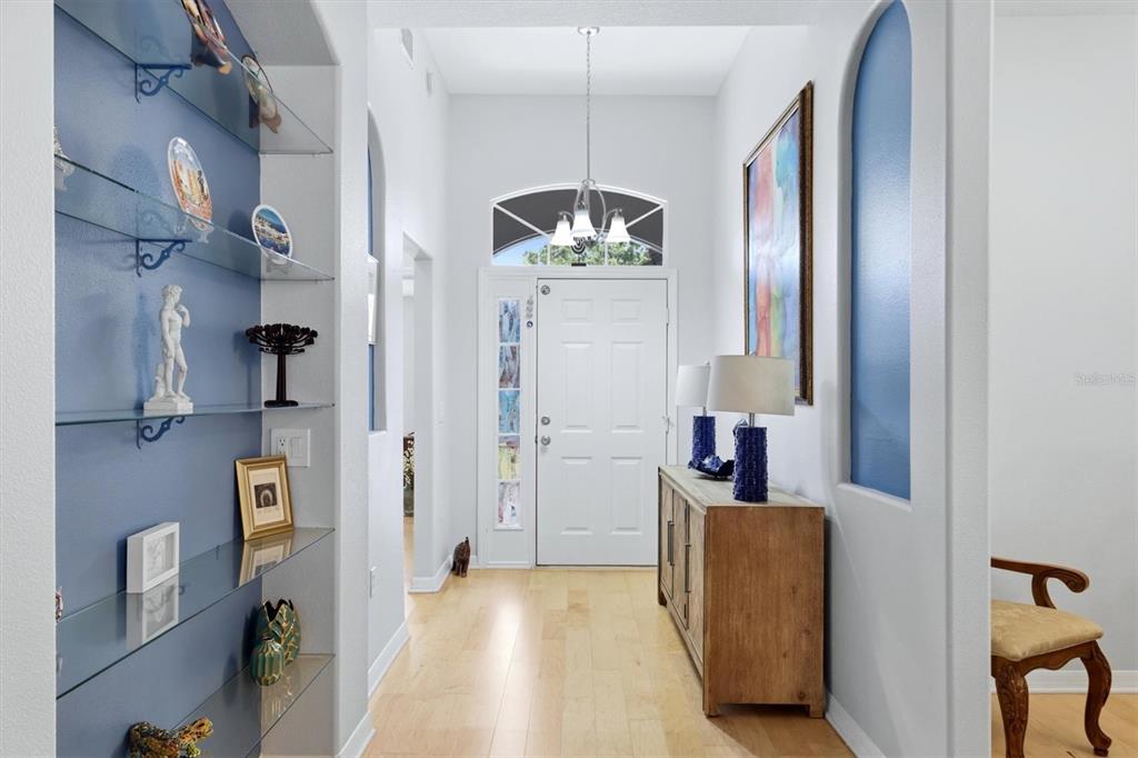 A bright entryway features light wood flooring, glass display shelves, and a white front door — 6726 W COUNTRY CLUB LANE, SARASOTA, FL