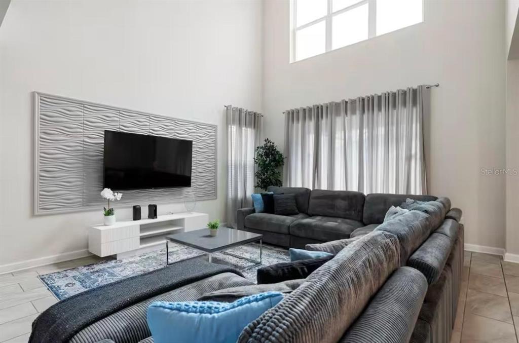 A living room features a textured accent wall, a large sectional sofa, and high ceilings — 2787 PUNCTUATION PLACE, KISSIMMEE, FL