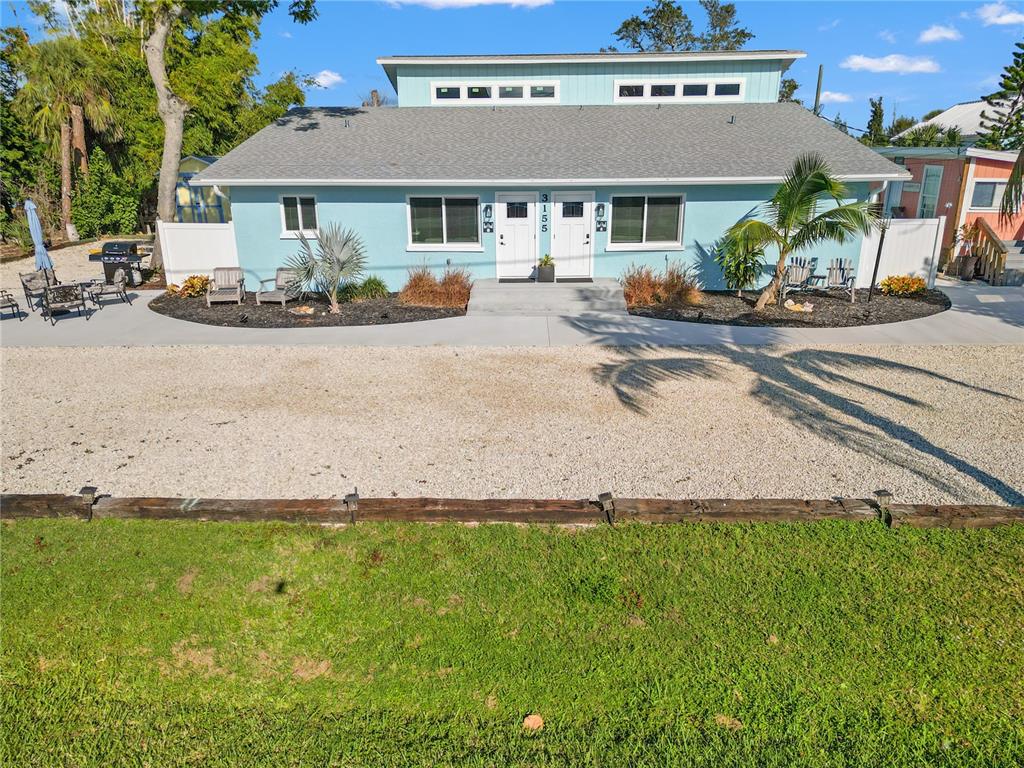 A light blue duplex with a gravel driveway and a grassy lawn in the foreground — 3155 WATERSIDE DRIVE, ENGLEWOOD, FL