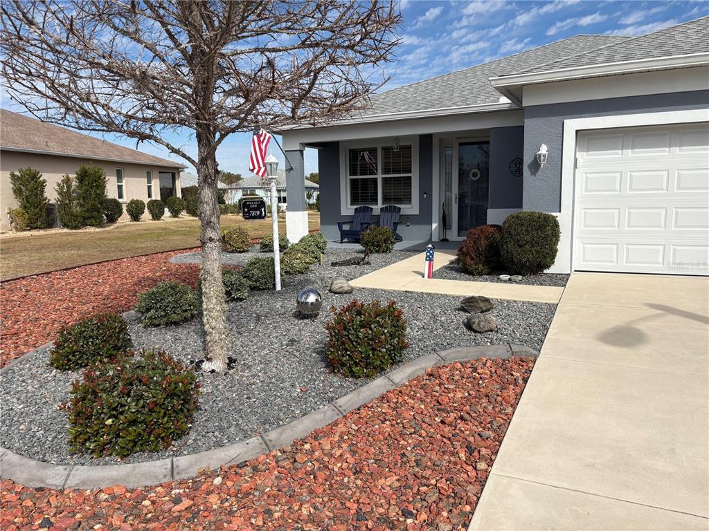 A gray house features a concrete driveway, a front porch, and a landscaped rock garden — 7819 SW 88TH STREET ROAD, OCALA, FL