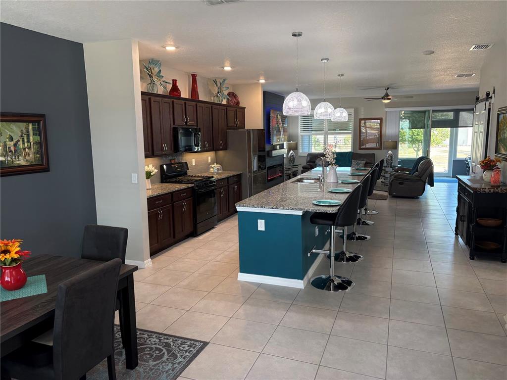 An open-concept kitchen features dark wood cabinets, a teal island, and granite countertops — 7819 SW 88TH STREET ROAD, OCALA, FL