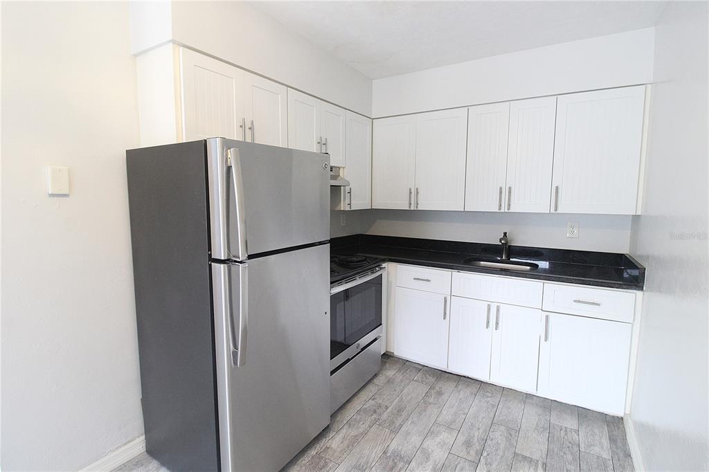 A kitchen features white cabinets, black countertops, stainless steel appliances, and wood-look tile flooring — 6383 GATEWAY AVENUE UNIT 6383, SARASOTA, FL