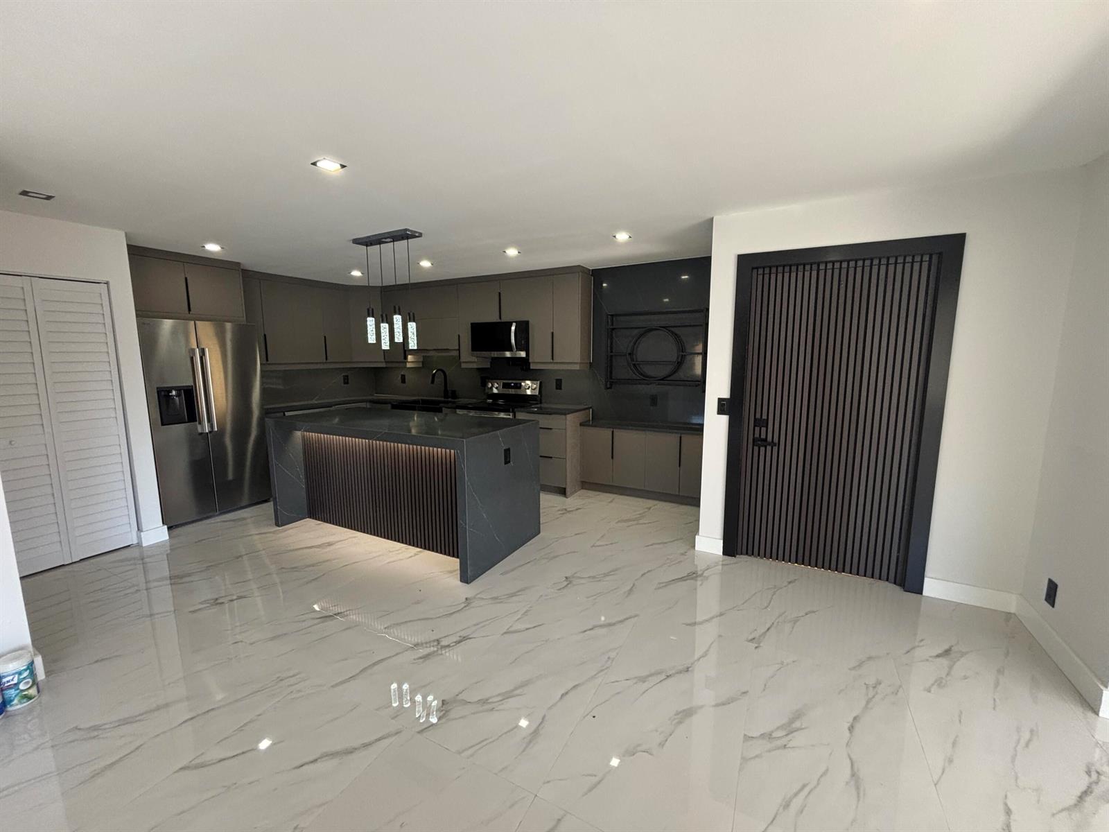 A modern kitchen features a dark stone island, gray cabinetry, and white marble-patterned tile floors — 4695 Sable Pine Circle # C2, West Palm Beach FL 33417, WEST PALM BEACH, FL