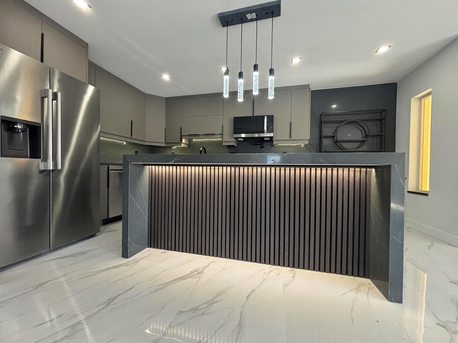 A modern kitchen features a dark stone waterfall island with slatted wood and under-cabinet lighting — 4695 Sable Pine Circle # C2, West Palm Beach FL 33417, WEST PALM BEACH, FL