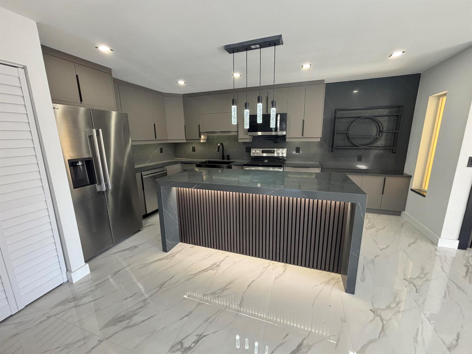 A modern kitchen features gray cabinetry, a dark stone waterfall island, and white marble flooring — 4695 Sable Pine Circle # C2, West Palm Beach FL 33417, WEST PALM BEACH, FL