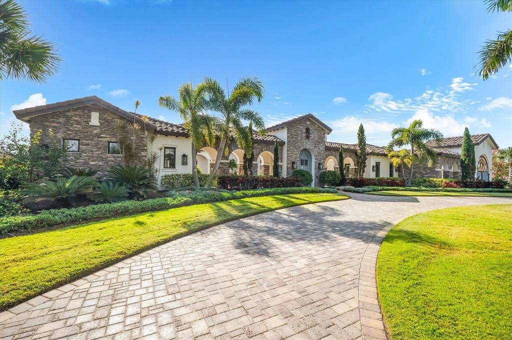 A stone-clad luxury home features a paved driveway and palm trees under a blue sky — 20906 PARKSTONE TERRACE, LAKEWOOD RANCH, FL