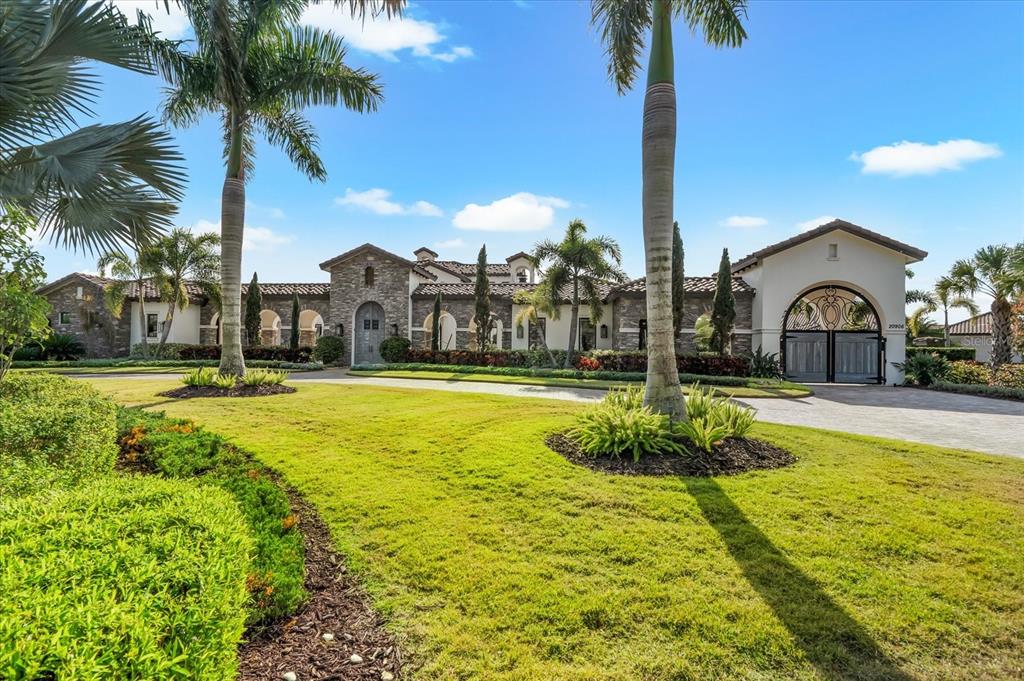 A sprawling Mediterranean-style estate features a stone facade, arched entryway, and a gated driveway — 20906 PARKSTONE TERRACE, LAKEWOOD RANCH, FL