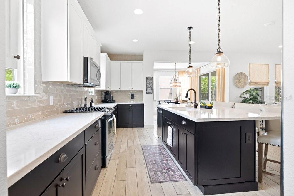 A kitchen features white upper cabinets, black lower cabinets, a large island, and light flooring — 15367 SHONAN GOLD DRIVE, WINTER GARDEN, FL