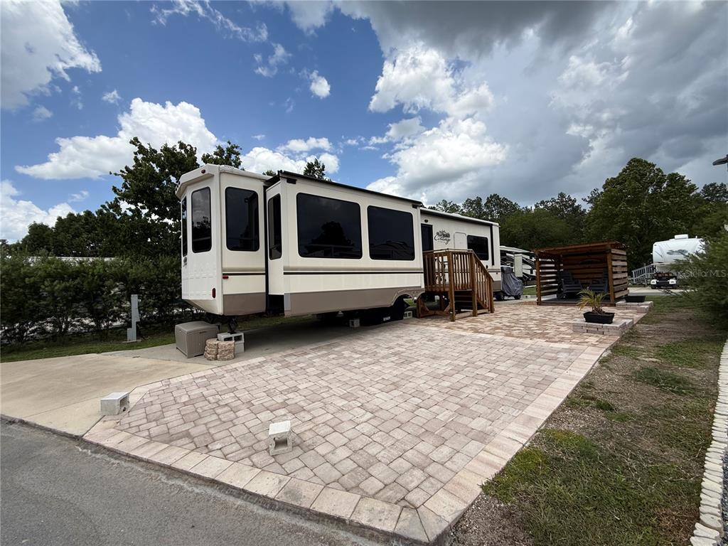 A parked recreational vehicle sits on a paved lot next to a wooden pergola — 2856 NE 104TH AVENUE, SILVER SPRINGS, FL