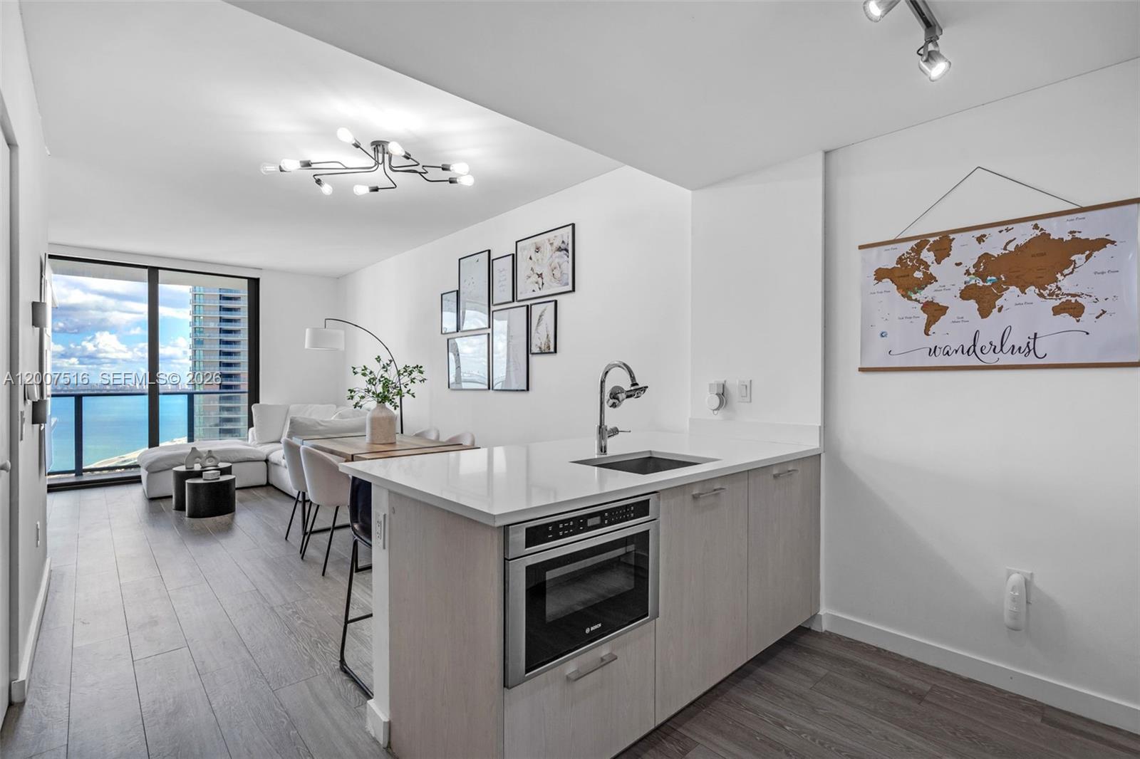 A modern kitchen with light wood cabinets and a microwave island overlooks a living area — 501 NE 31st St # 3704, Miami FL 33137, MIAMI, FL