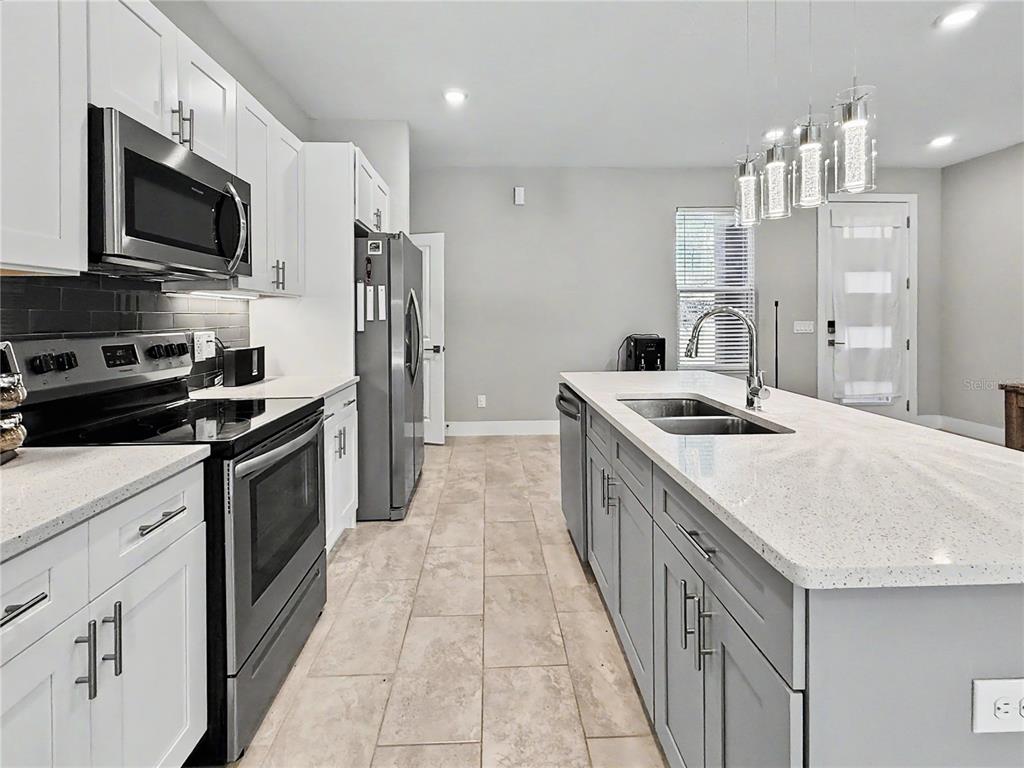 A modern kitchen features white upper cabinets, gray lower cabinets, stainless steel appliances, and a quartz-topped island — 4667 BRASHER AVENUE, NORTH PORT, FL