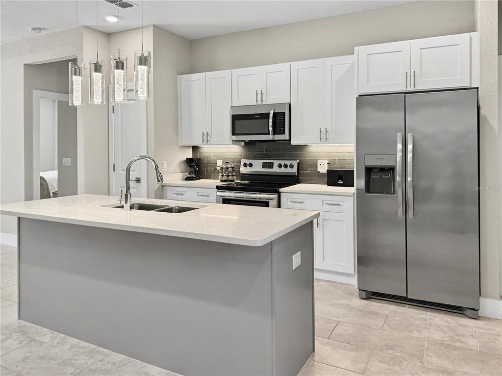 A modern kitchen features white cabinets, stainless steel appliances, a gray island, and tile flooring — 4667 BRASHER AVENUE, NORTH PORT, FL