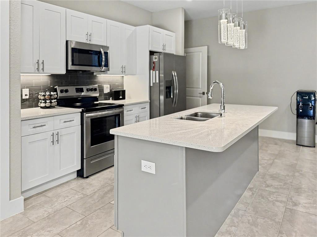 A modern kitchen features white cabinets, stainless steel appliances, a gray island, and tile flooring — 4667 BRASHER AVENUE, NORTH PORT, FL