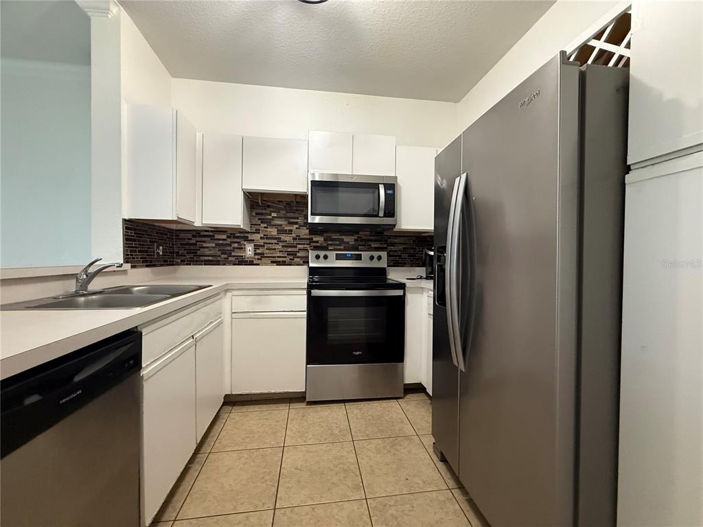 A kitchen features white cabinets, stainless steel appliances, a tiled backsplash, and light-colored floor tiles — 2674 ROBERT TRENT JONES DRIVE UNIT 337, ORLANDO, FL