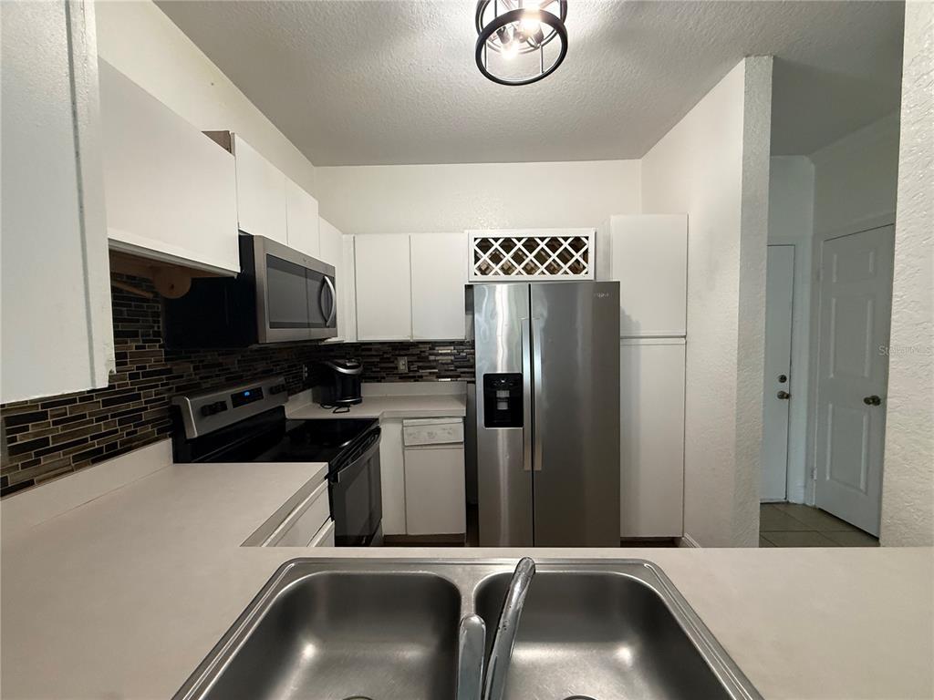A kitchen features white cabinets, stainless steel appliances, a tiled backsplash, and a double sink — 2674 ROBERT TRENT JONES DRIVE UNIT 337, ORLANDO, FL