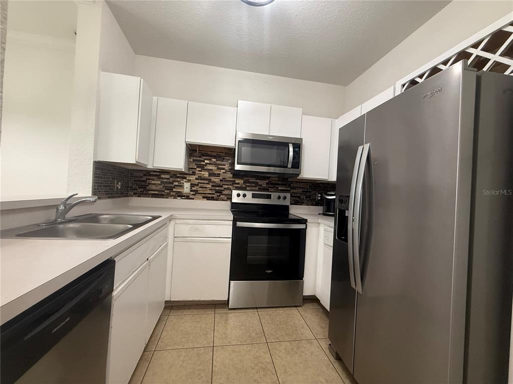A kitchen features white cabinets, stainless steel appliances, a tiled backsplash, and light-colored countertops — 2674 ROBERT TRENT JONES DRIVE UNIT 337, ORLANDO, FL