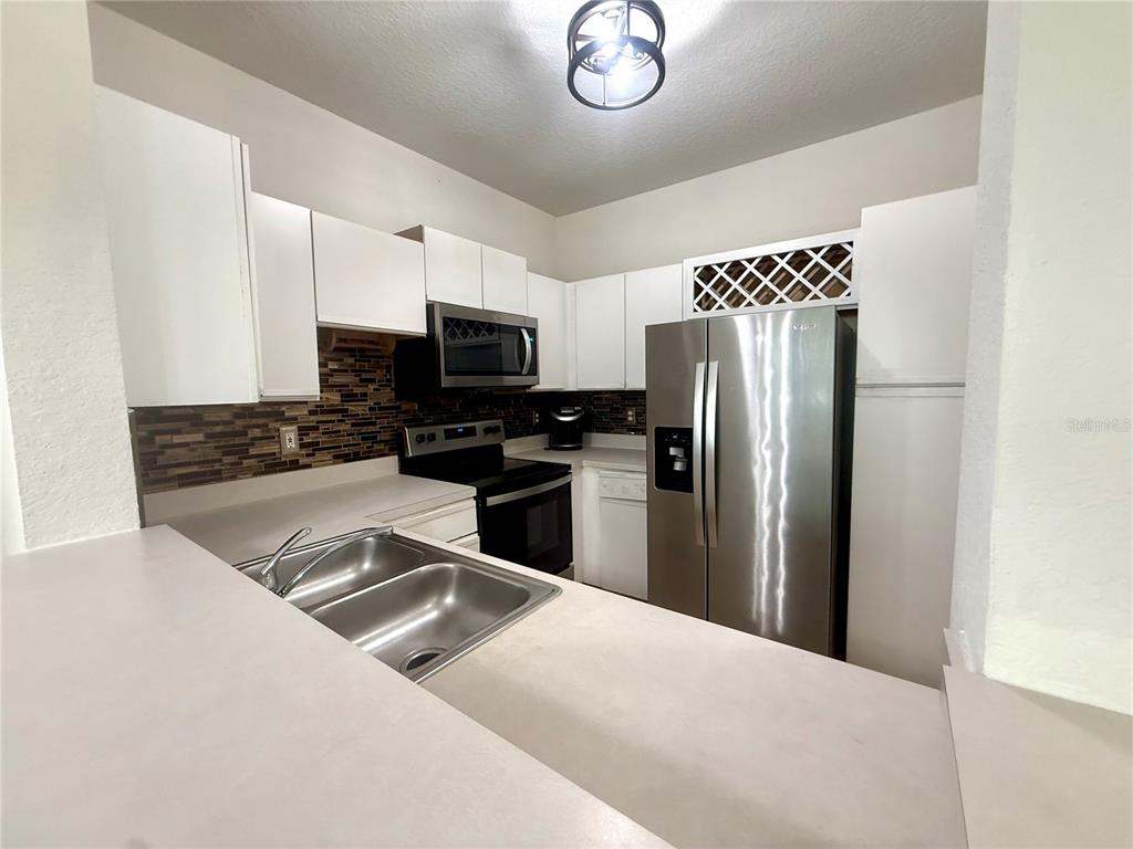 A kitchen features white cabinets, stainless steel appliances, a double sink, and a tiled backsplash — 2674 ROBERT TRENT JONES DRIVE UNIT 337, ORLANDO, FL