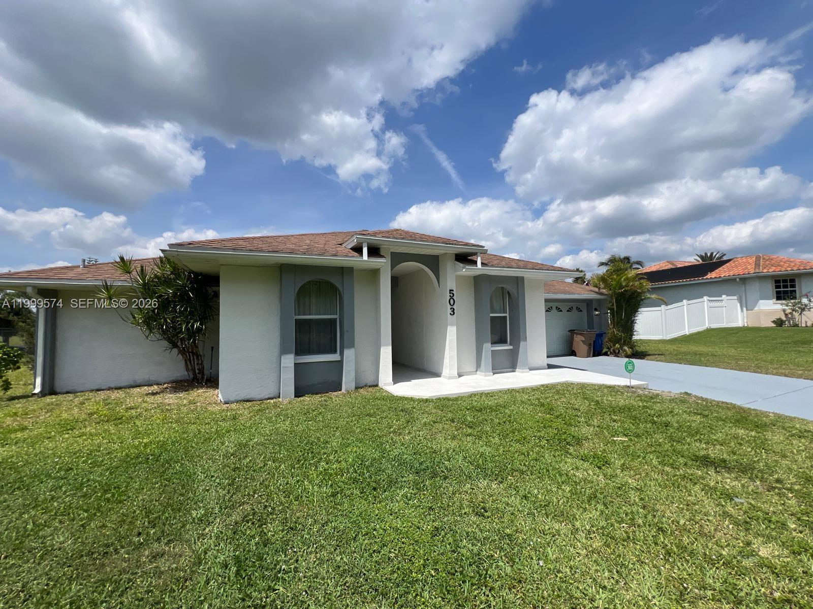 A single-story house with a white stucco exterior, gray accents, and a brown shingled roof — 503 Jackson Ave, Lehigh Acres FL 33972, LEHIGH ACRES, FL