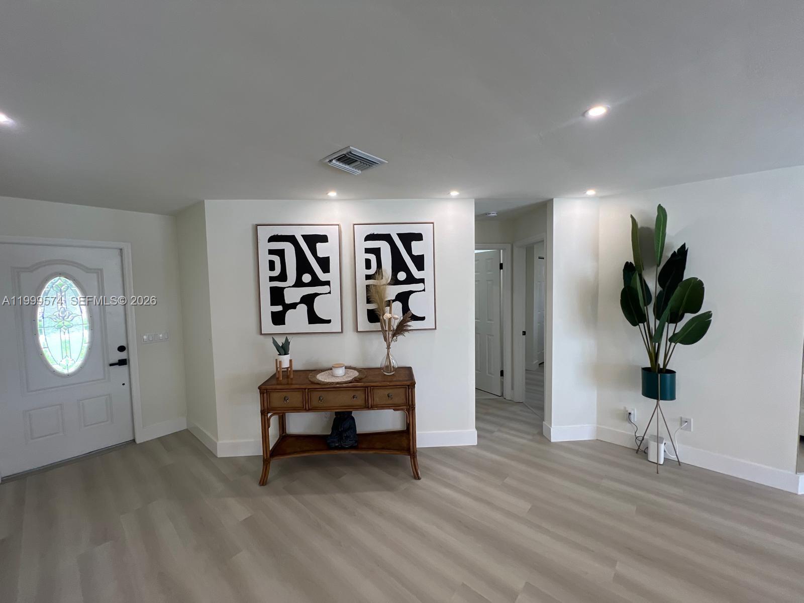 An entryway features light wood-look flooring, a wooden console table, two abstract art pieces, and a plant — 503 Jackson Ave, Lehigh Acres FL 33972, LEHIGH ACRES, FL