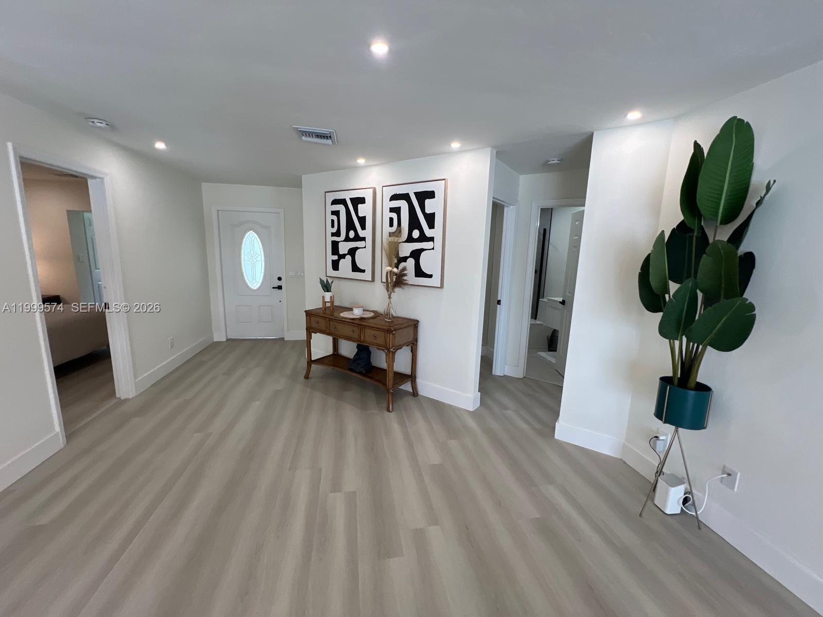 An entryway features light wood-look flooring, a wooden console table, and two abstract wall art pieces — 503 Jackson Ave, Lehigh Acres FL 33972, LEHIGH ACRES, FL