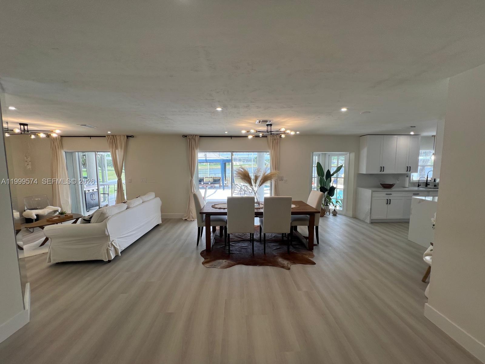 An open-concept living and dining area features light wood flooring, white cabinetry, and sliding doors — 503 Jackson Ave, Lehigh Acres FL 33972, LEHIGH ACRES, FL