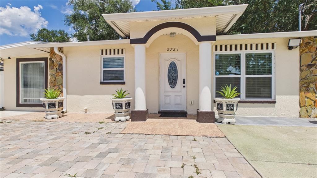 The exterior of a single-story house features a paved driveway, white columns, and potted plants — 8721 N ORANGEVIEW AVENUE, TAMPA, FL