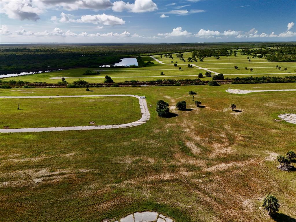 An aerial view shows a large, undeveloped grassy lot with paved roads and distant trees — 12392 BONITA PLACE, PLACIDA, FL