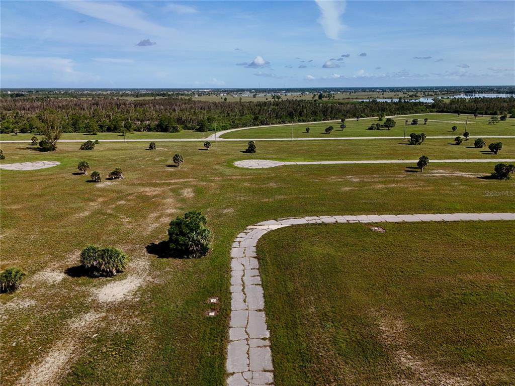 An aerial view shows a paved road curving through a large, undeveloped grassy field — 12392 BONITA PLACE, PLACIDA, FL