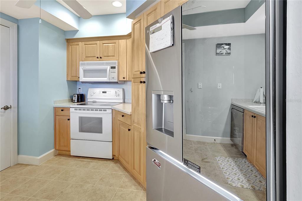 A kitchen features light wood cabinets, white appliances, a stainless steel refrigerator, and tiled floors — 3191 MATECUMBE KEY ROAD UNIT 607, PUNTA GORDA, FL