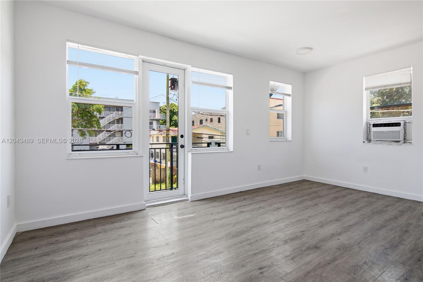 An empty room features white walls, gray wood-look flooring, a balcony door, and windows — 402 NW 12th Ave # 205, Miami FL 33128, MIAMI, FL