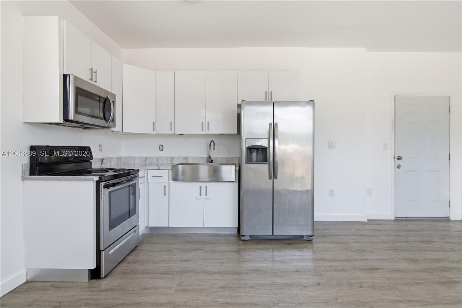 A kitchen features white cabinets, stainless steel appliances, a farmhouse sink, and wood-look flooring — 402 NW 12th Ave # 205, Miami FL 33128, MIAMI, FL