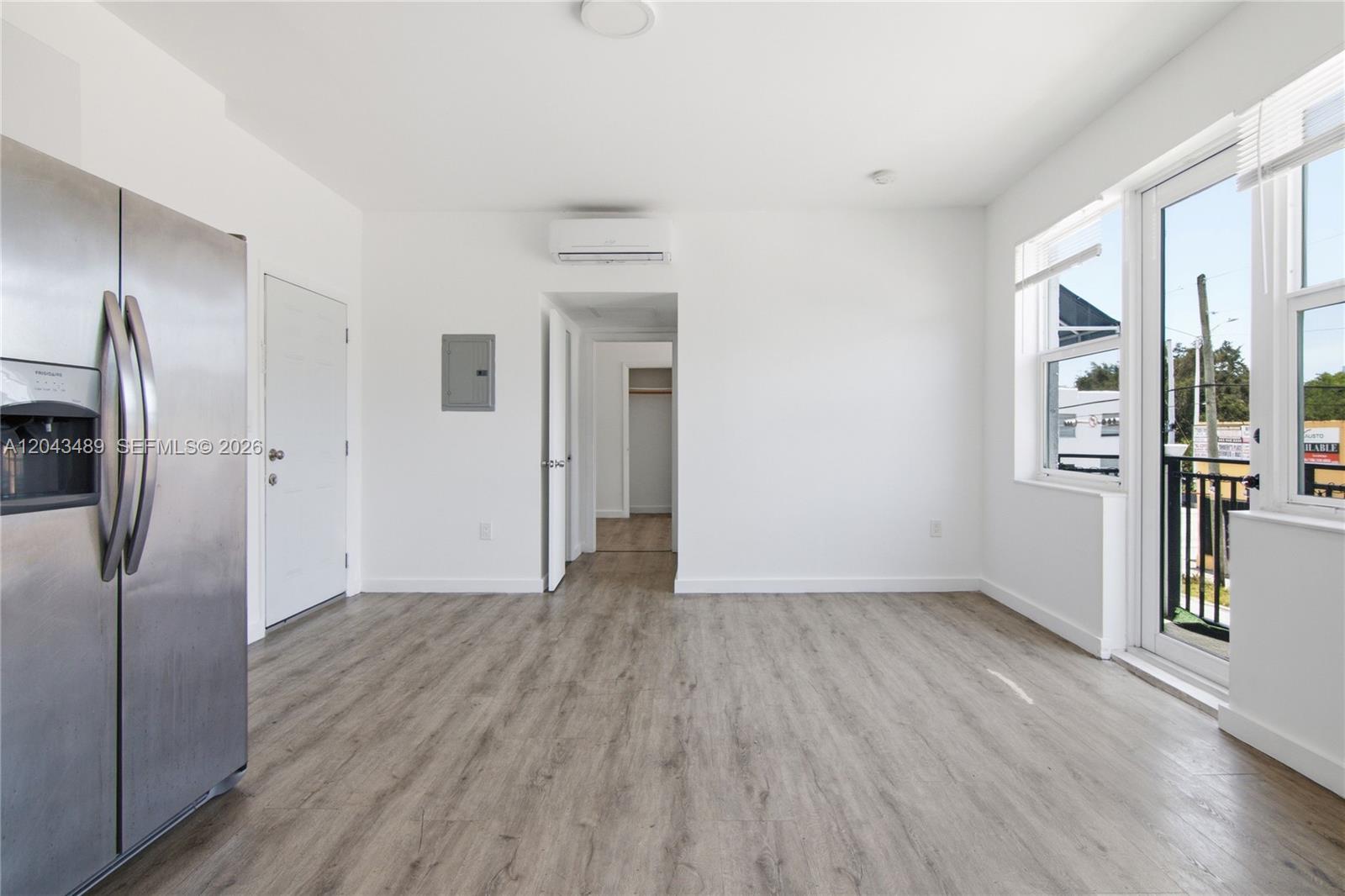 An empty room features light wood-look flooring, white walls, a stainless steel refrigerator, and a balcony — 402 NW 12th Ave # 205, Miami FL 33128, MIAMI, FL