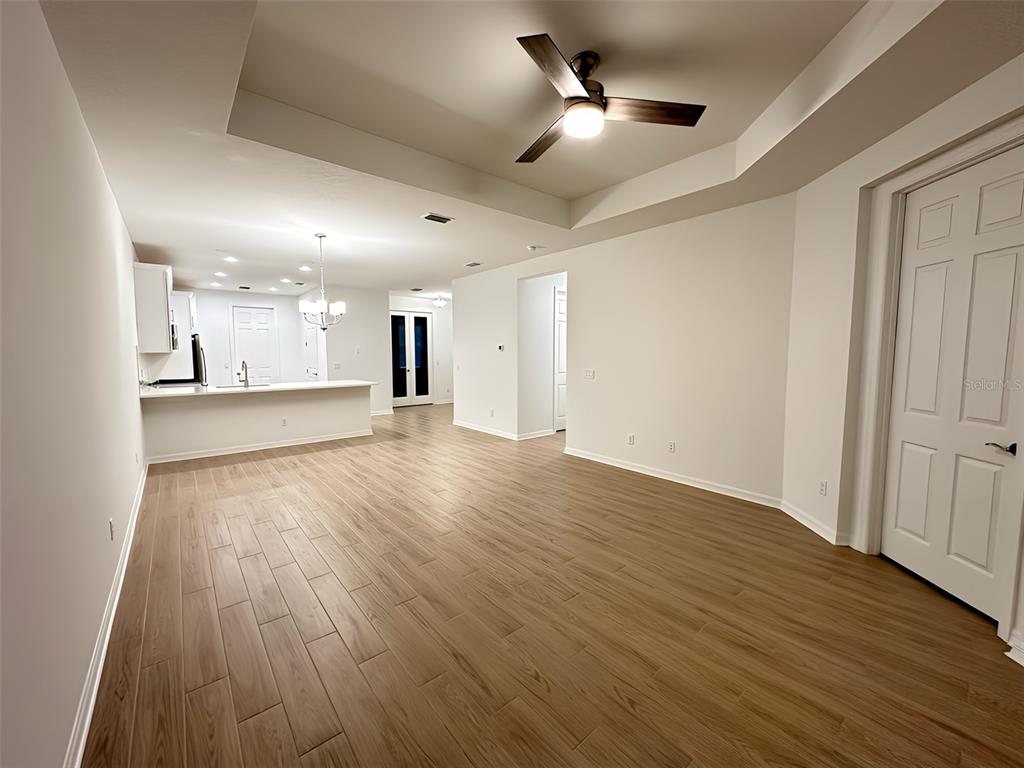 An open-concept living area features light wood-look tile flooring, a tray ceiling, and a kitchen — 17929 CHERISHED LOOP, LAKEWOOD RANCH, FL