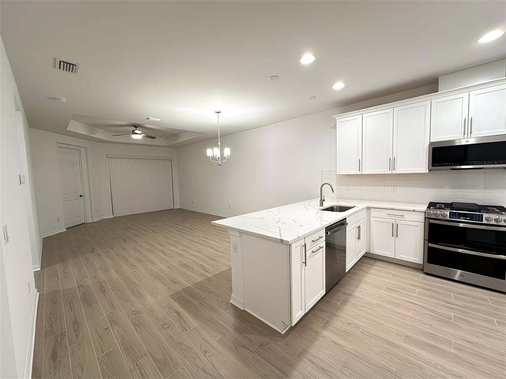 A kitchen with white cabinets, a marble-topped island, and light wood-look tile flooring — 17929 CHERISHED LOOP, LAKEWOOD RANCH, FL