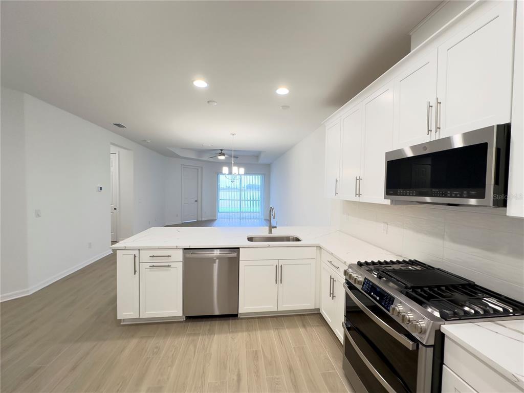 A modern kitchen features white cabinets, stainless steel appliances, and a large quartz island — 17929 CHERISHED LOOP, LAKEWOOD RANCH, FL