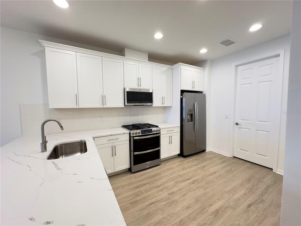 A modern kitchen features white cabinets, stainless steel appliances, and a white marble-look countertop — 17929 CHERISHED LOOP, LAKEWOOD RANCH, FL