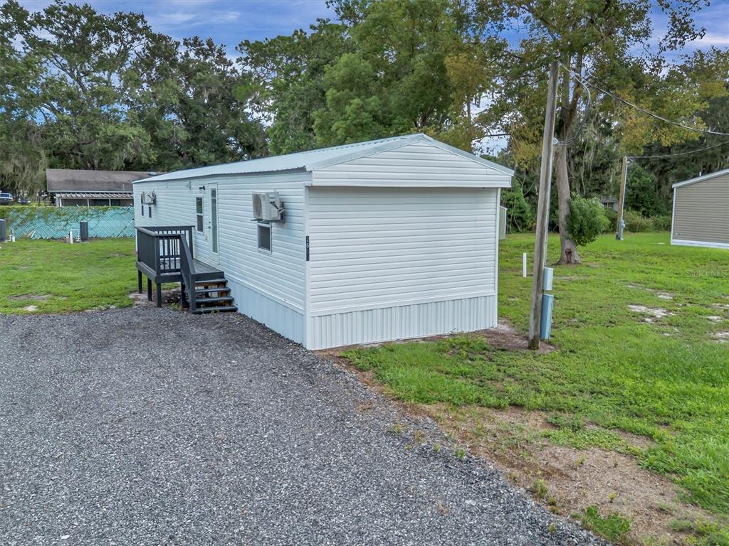 A white mobile home sits on a gravel lot with a small wooden deck — 2667 SNAPPING TURTLE DRIVE, LAKE WALES, FL