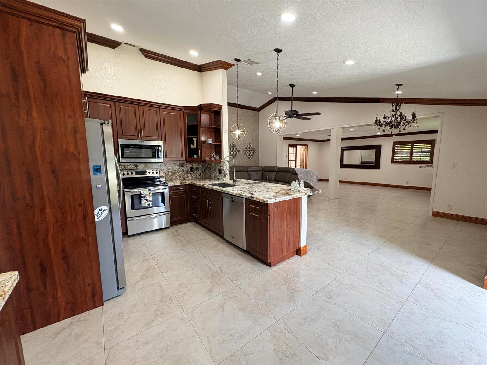 A kitchen with dark wood cabinets, granite countertops, and tile flooring opens to a living area — 15943 W Wind Circle, Sunrise FL 33326, SUNRISE, FL