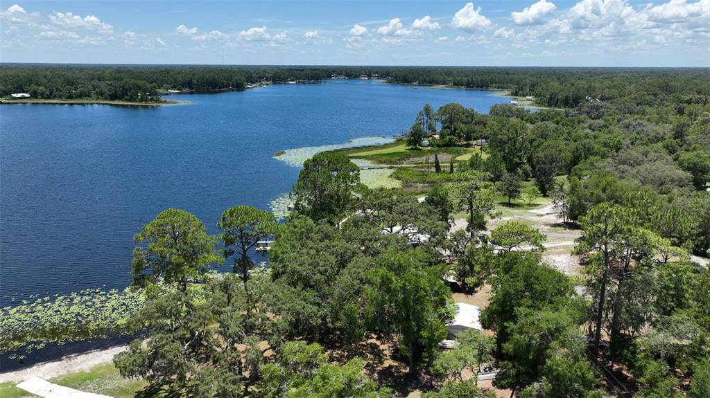 An aerial view shows a large lake surrounded by dense trees and grassy shoreline areas — 104 CARTER WHITTAKER LANE, POMONA PARK, FL