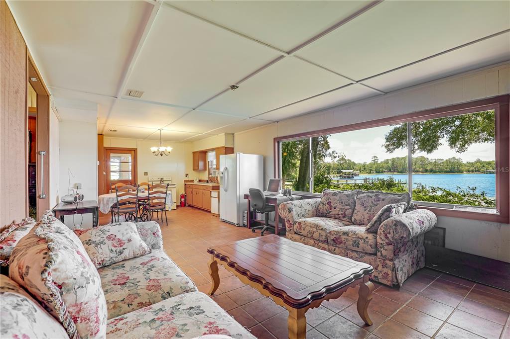 A living room and kitchen area with tile floors, floral sofas, and a large lake view — 104 CARTER WHITTAKER LANE, POMONA PARK, FL