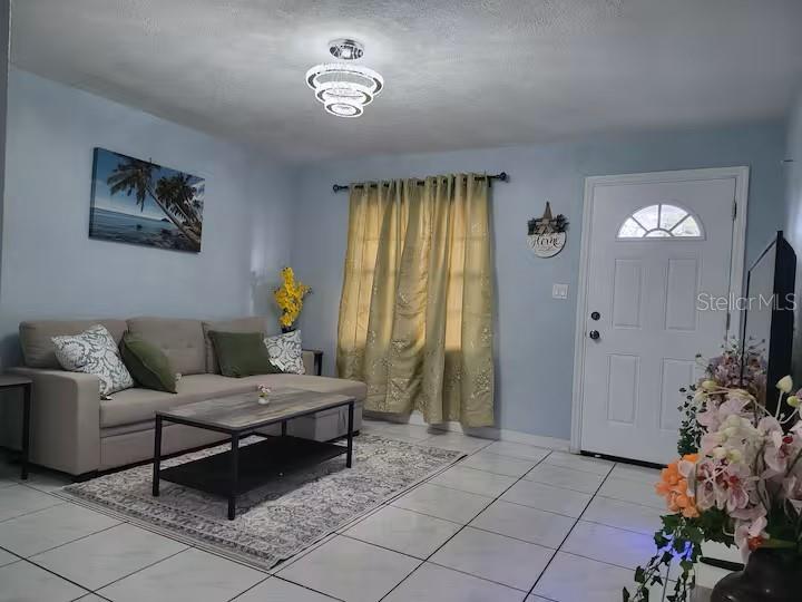 A living room features light blue walls, tile flooring, a sofa, and a modern chandelier — 3552 38TH AVENUE N, ST PETERSBURG, FL