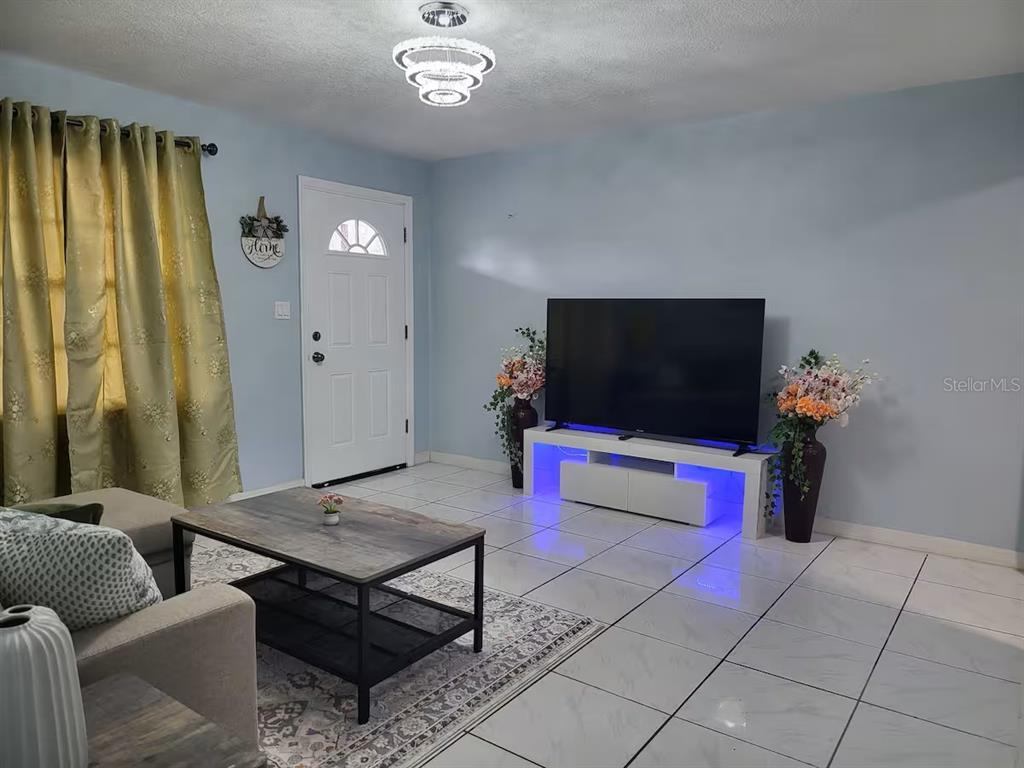 A living room features light blue walls, white tile flooring, a TV console, and a rug — 3552 38TH AVENUE N, ST PETERSBURG, FL