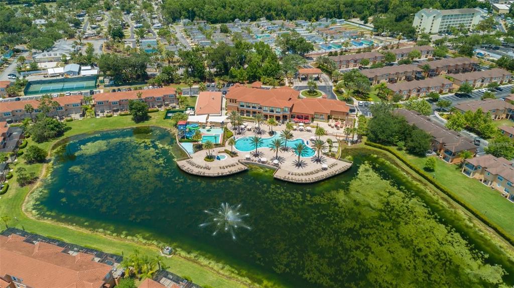 An aerial view shows a community clubhouse with a pool and fountain on a lake — 2665 TRIUMPH WAY, KISSIMMEE, FL