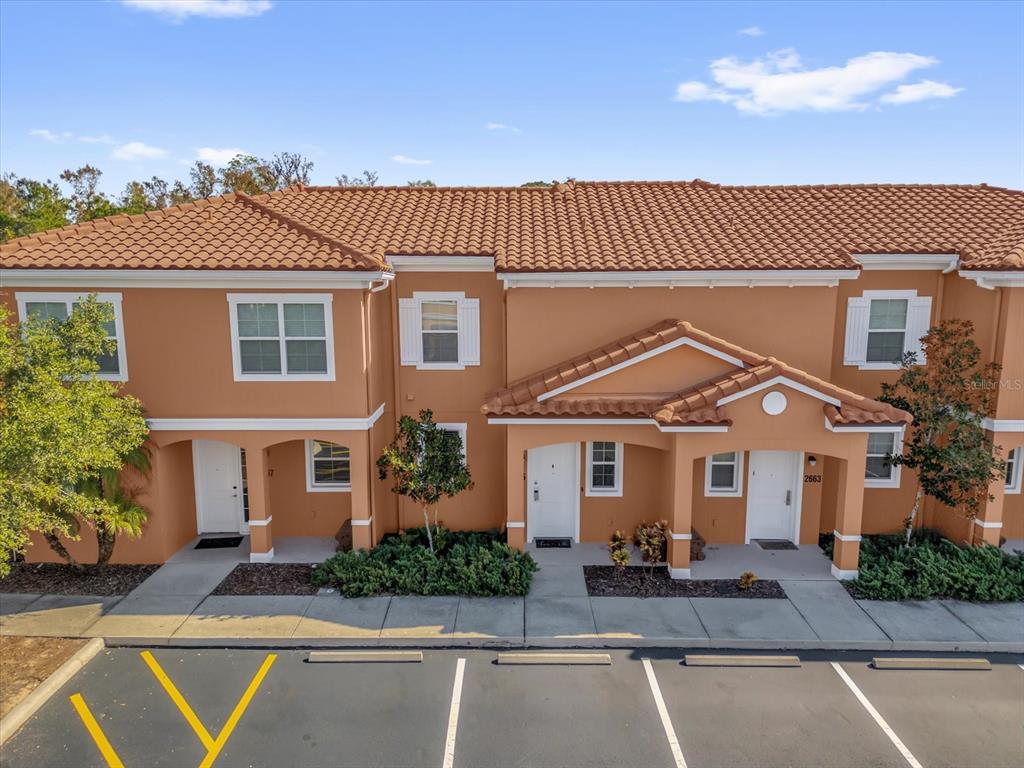 An exterior view of a two-story tan townhouse complex with a tiled roof and parking — 2665 TRIUMPH WAY, KISSIMMEE, FL