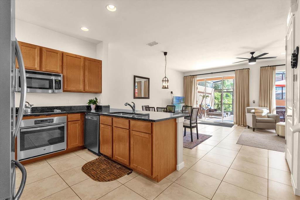 A kitchen with wood cabinets and stainless appliances opens to a living area with patio access — 2665 TRIUMPH WAY, KISSIMMEE, FL