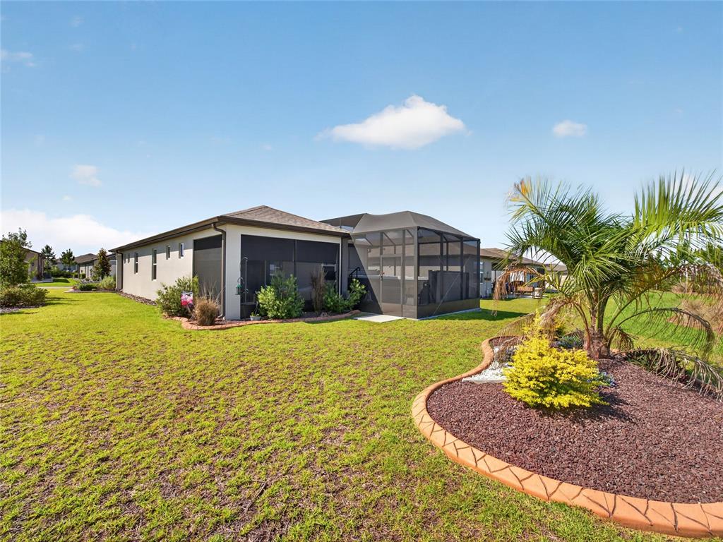 A backyard view of a house with a screened-in lanai and a landscaped garden bed — 5798 SW 86TH AVENUE ROAD, OCALA, FL