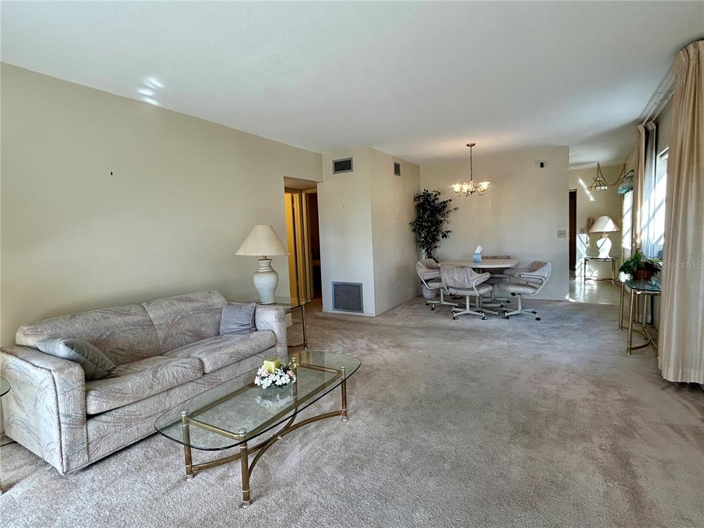 A living and dining area with beige carpet, a patterned sofa, and a glass coffee table — 2464 AUSTRALIA WAY E UNIT 78, CLEARWATER, FL