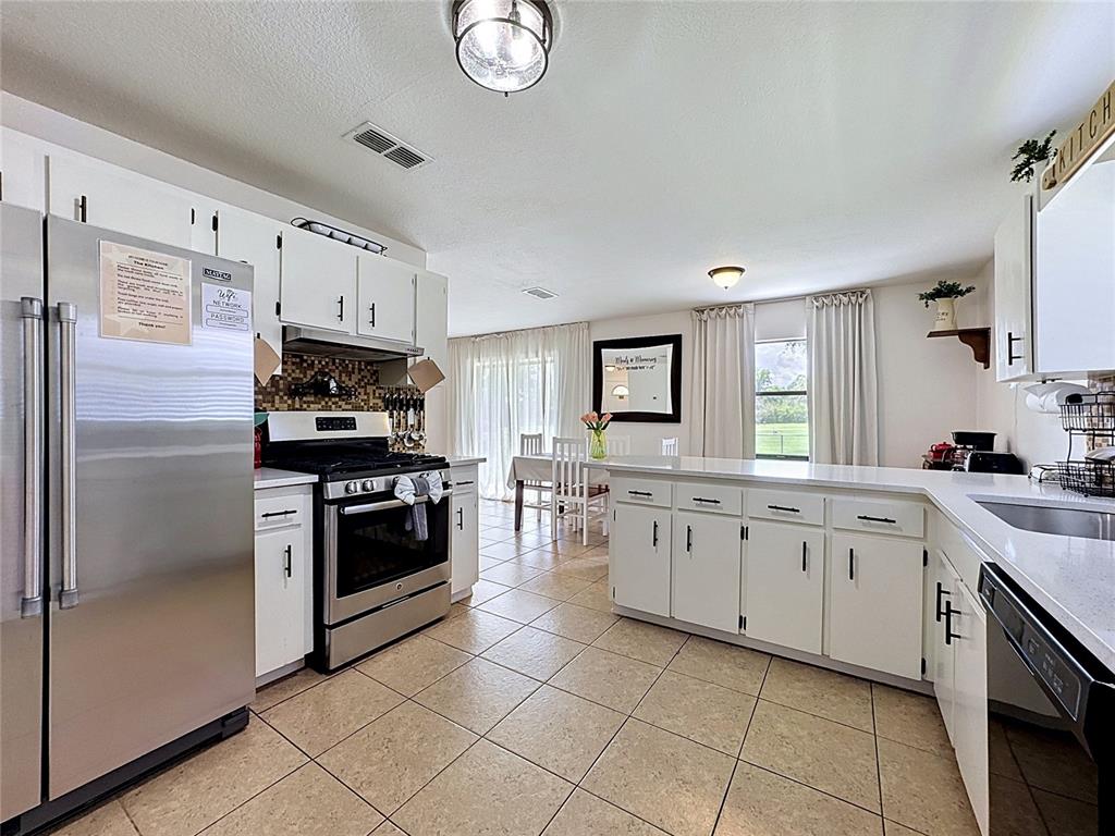 A kitchen with white cabinets, stainless steel appliances, and tile flooring opens to a dining area — 1716 TERRY CIRCLE NE, WINTER HAVEN, FL