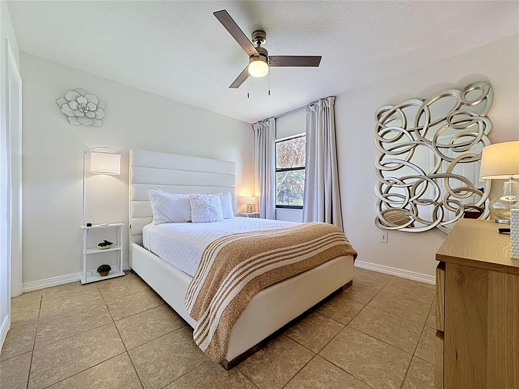 A bedroom features a white upholstered bed, tile flooring, a ceiling fan, and wall decor — 1716 TERRY CIRCLE NE, WINTER HAVEN, FL